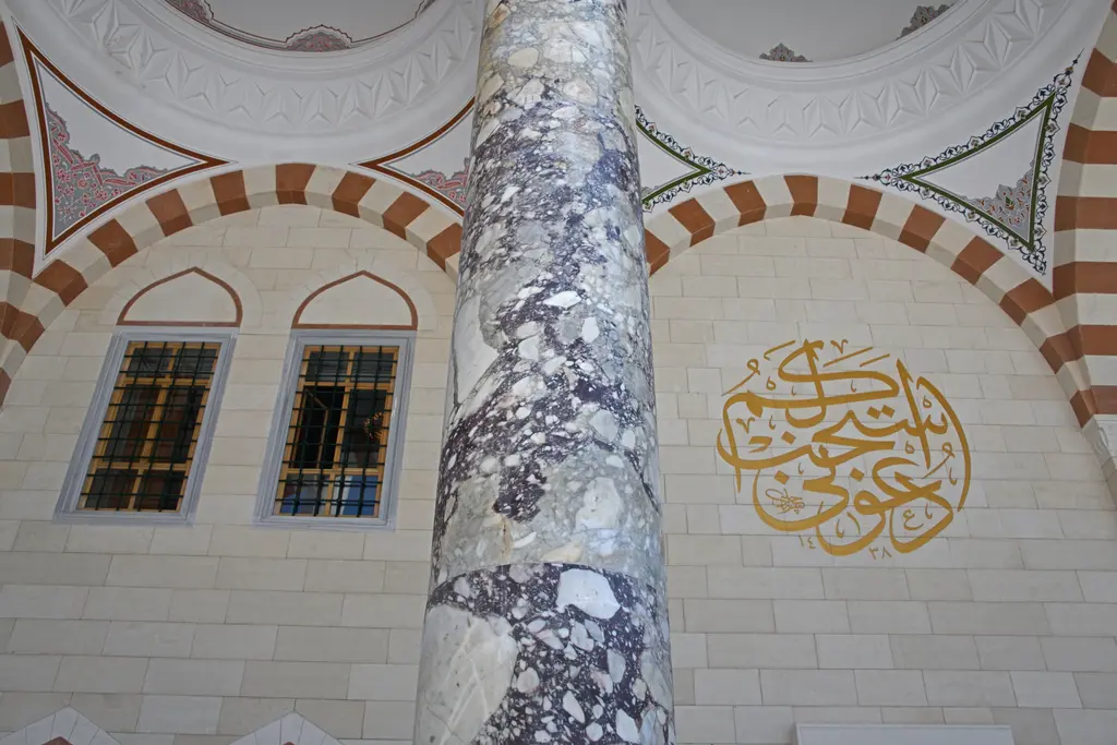 Büyük Çamlıca Camii'nde revak; damarlı mermer sütun, kırmızı beyaz kemerler ve duvarda altın renkli hat.