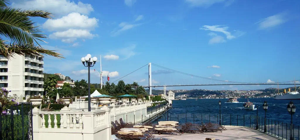 Çırağan Sarayı'ndan Boğaz; ön planda kıyı terası ve palmiye, ortada su, uzakta köprü ve karşı kıyı.