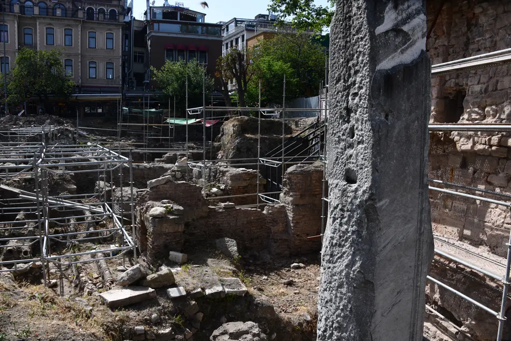 Sultanahmet'te Milyon Taşı; önde aşınmış mermer ayak, arkada iskeleler arasında Bizans duvar kalıntıları ve tuğla örgülü su terazisi.