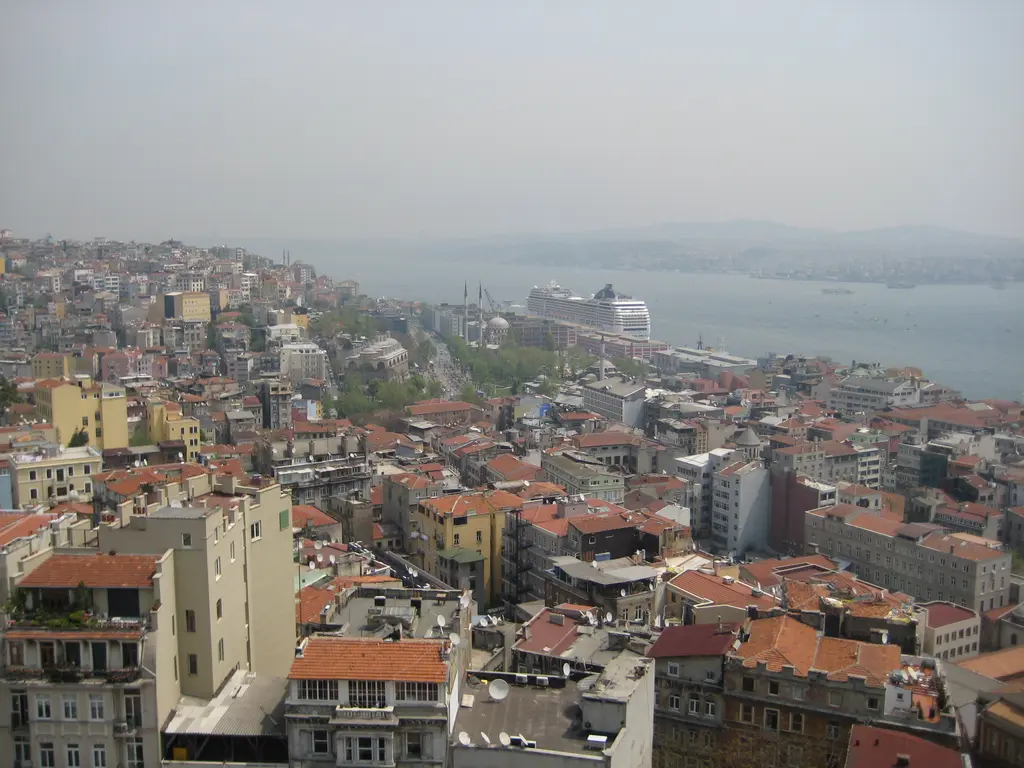 Cihangir'den aşağıya bakış; kiremit çatılar, kıyı boyunca ağaçlı yol, rıhtımda yolcu gemisi ve uzakta Asya yakası.
