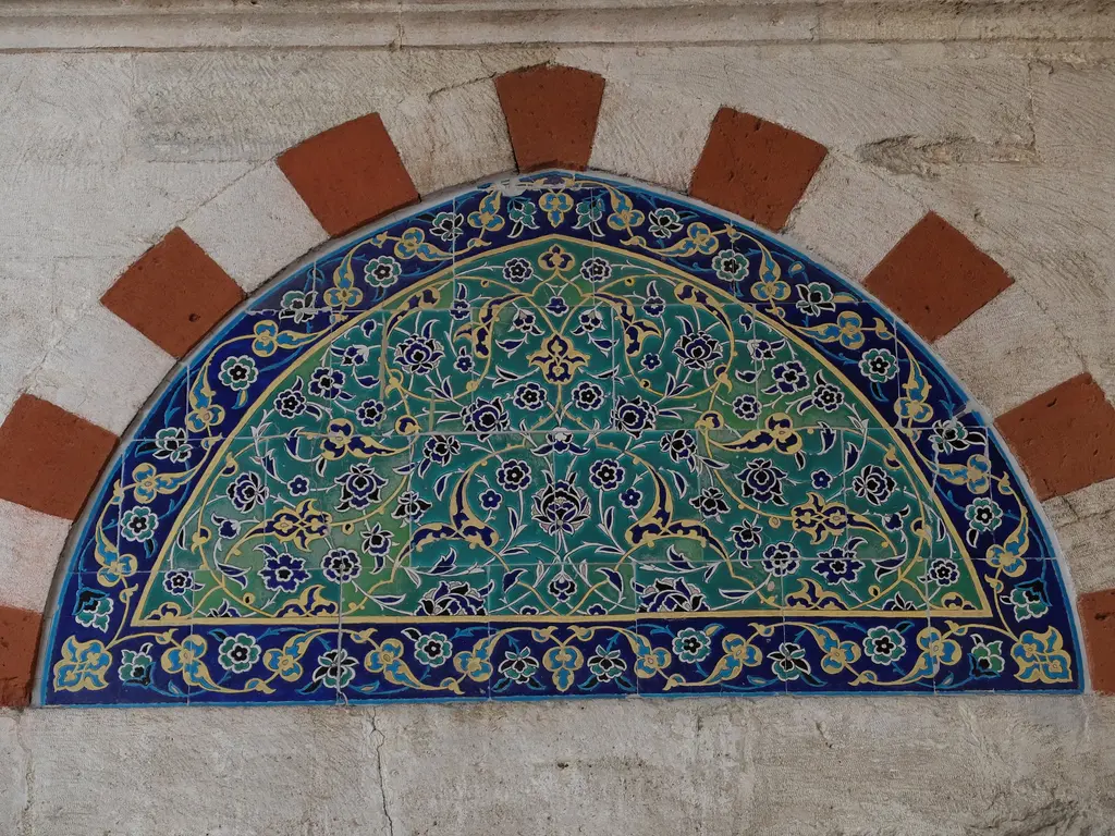 Yavuz Sultan Selim Camii'nde pencere alınlığı; kırmızı beyaz almaşık taş kemerin içinde yeşil, turkuaz ve lacivert renkli yarım daire çini pano.