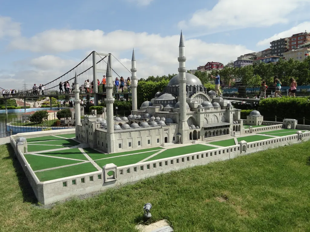 Miniatürk'te Süleymaniye Camii maketi; dört minare, yeşil zeminli avlu ve gri duvarlar, solda asma köprü maketi ve ziyaretçiler.