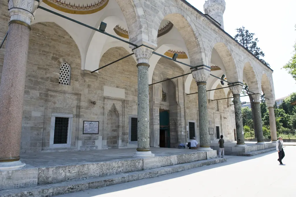 Murat Paşa Camii revakı; sıralı sütunlar, sivri kemerler, taş cephede pencereler ve mihrap nişleri, önde geniş taş zemin.