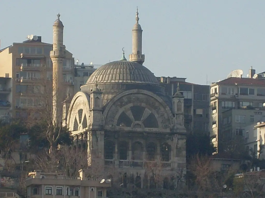 Cihangir Camii'ne denizden yakın bakış; kubbe, yarım daire pencereli cephe, iki ince minare ve çevresindeki apartmanlar.