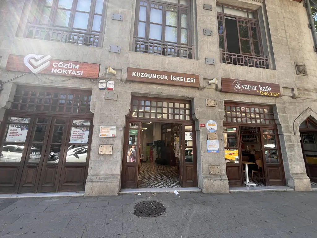 Kuzguncuk İskelesi; taş cepheli iki katlı bina, kemerli kapılar, cam bölmeli giriş ve üstte iskele tabelası.