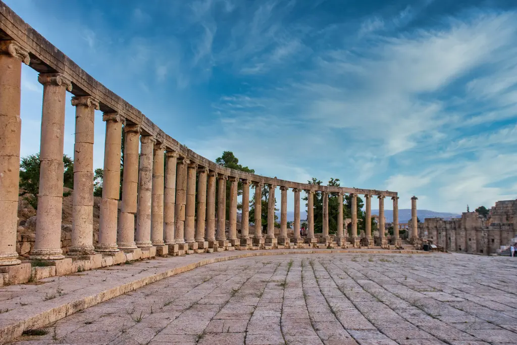 Jerash'ta yan yana dizilmiş yüksek taş sütunlar; başlıkları korunmuş sütun sırası, taş döşeli geniş meydan ve bulutlu mavi gökyüzü.