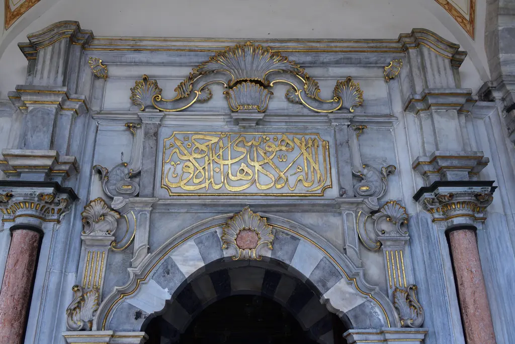 Mihrişah Valide Sultan Türbesi'nin kapısı; siyah-beyaz mermer kemer, yaldızlı yazı kuşağı, istiridye motifli taç ve pembe mermer sütunlar.