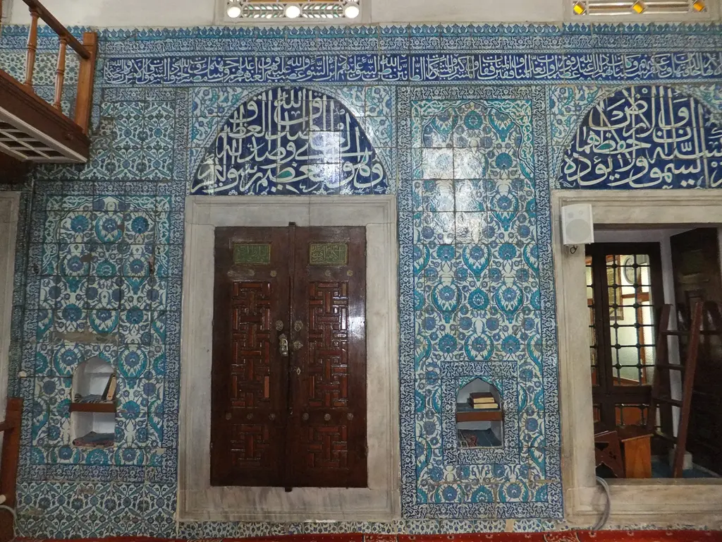 Çinili Camii'nde giriş duvarı; ahşap kapı, mavi çinili yüzey, yazılı alınlıklar ve solda ahşap mahfil.