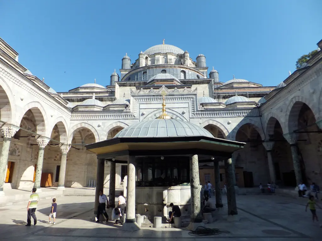 Beyazıt Camii'nin avlusu; revaklı galeriler, ortada kubbeli şadırvan, mermer zemin ve arkada caminin gövdesi ile kubbeleri.