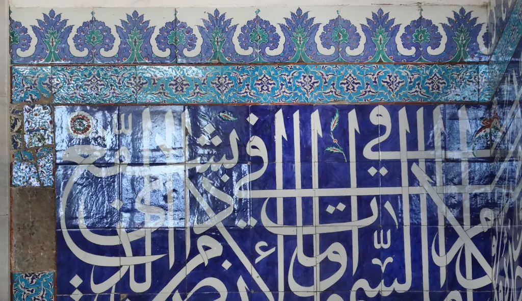 Atik Valide Camii'nde çini pano; lacivert zemin üzerinde beyaz celi yazı ve üstte çiçek motifli bordür.