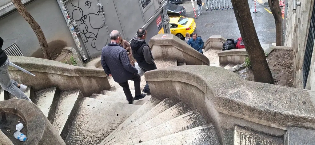Kamondo Merdivenleri'nden inen insanlar; geniş açıyla kıvrımlı basamaklar, korkuluktaki duvar yazıları ve aşağıda sokak.