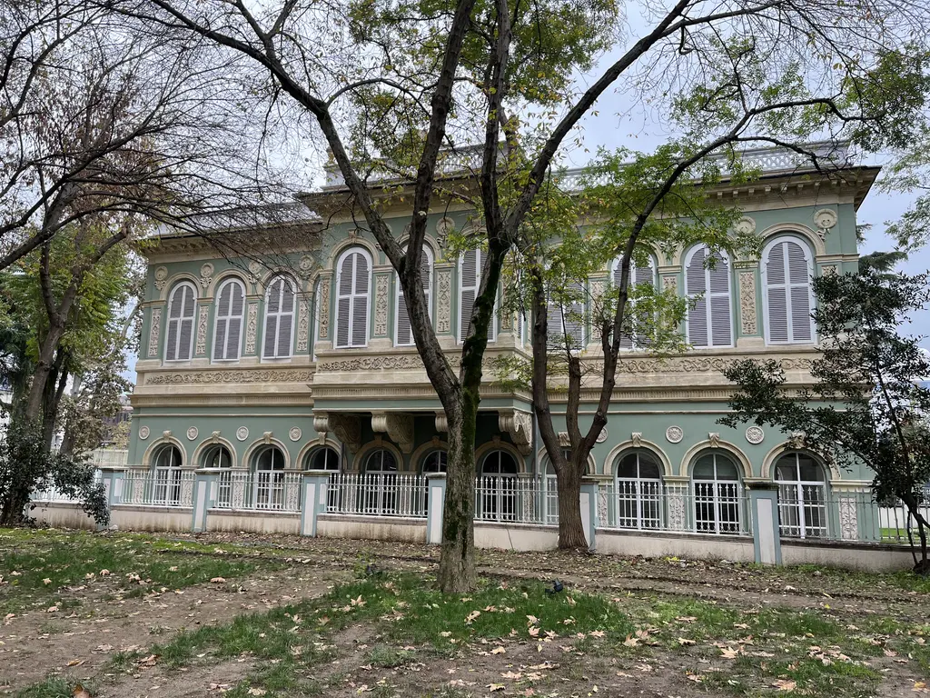 Tophane Kasrı'nın bahçesi; yeşil cepheli köşk, önünde budanmış ağaçlar ve demir parmaklıklı bahçe duvarı.