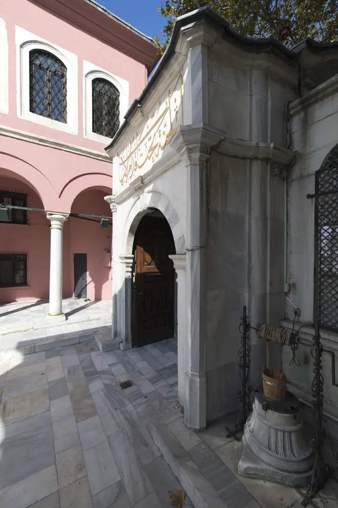Şah Sultan Külliyesi'nde avludan kapı; dalgalı saçaklı mermer kapı, pembe mektep binası ve önde bir kuyu bileziği.
