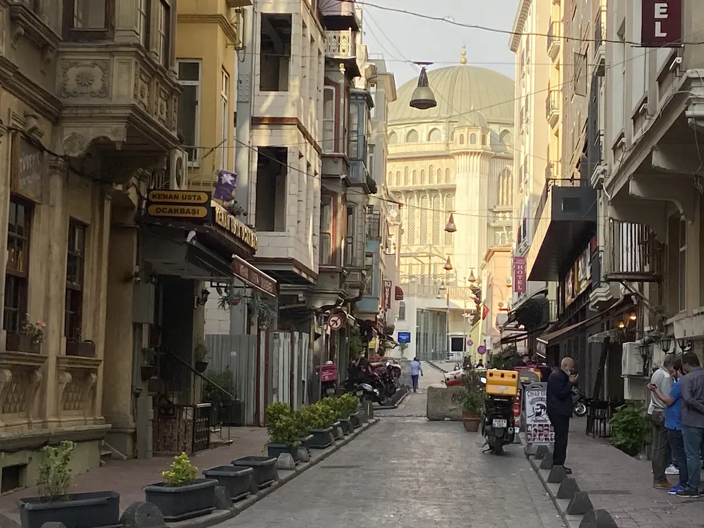 Beyoğlu'nda dar bir sokak; iki yanda cumbalı eski apartmanlar ve kafeler, sokağın ucunda Taksim Camii'nin kubbesi.
