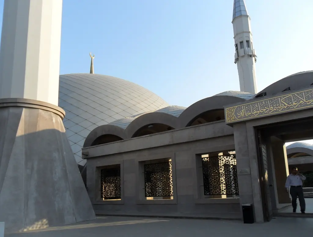 Şakirin Camii; beton minare kaidesi, gümüş renkli kubbe, kemerli revak çatıları ve arkada yükselen ince minare.
