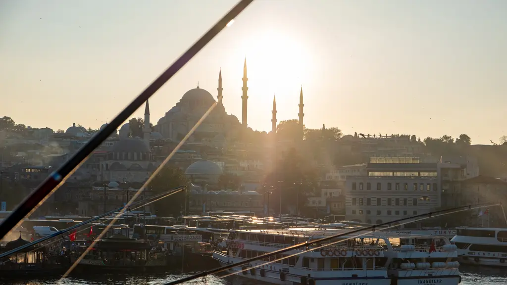 Gün batımında köprüden Süleymaniye; güneşin önünde cami siluetleri, oltaların çapraz çizgileri ve parlayan su.