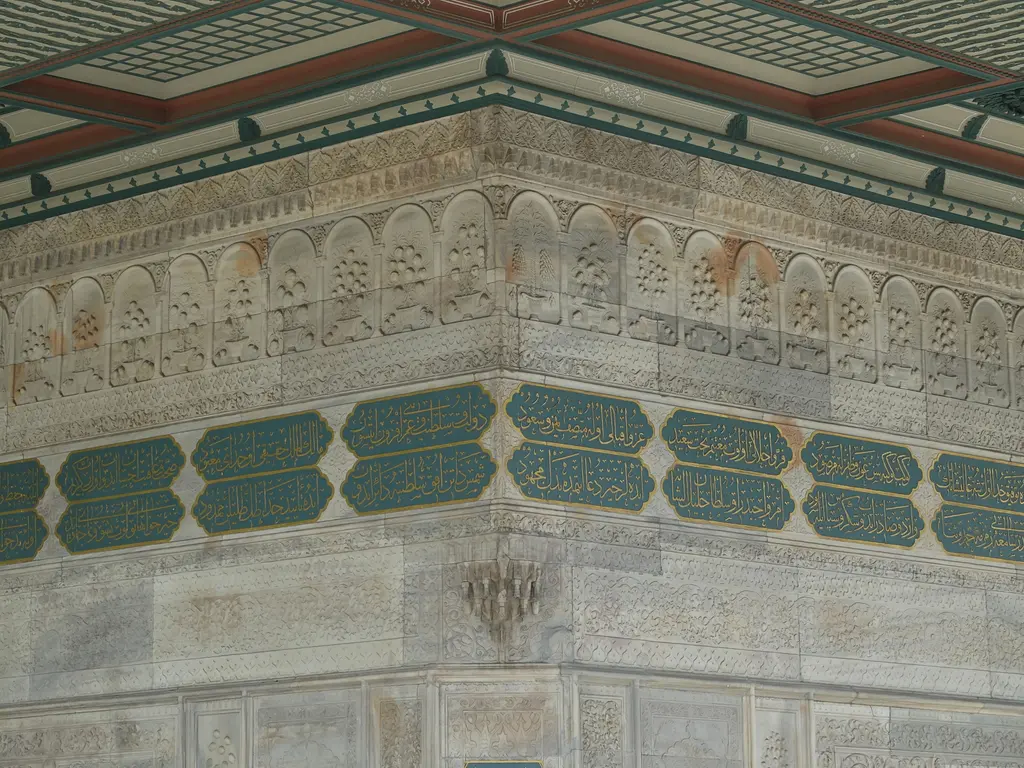Tophane Çeşmesi'nin bir köşesi; yeşil zeminli kartuşlar halinde kitabe kuşağı, üstte kemerli nişlerde kabartmalar ve saçak altı.