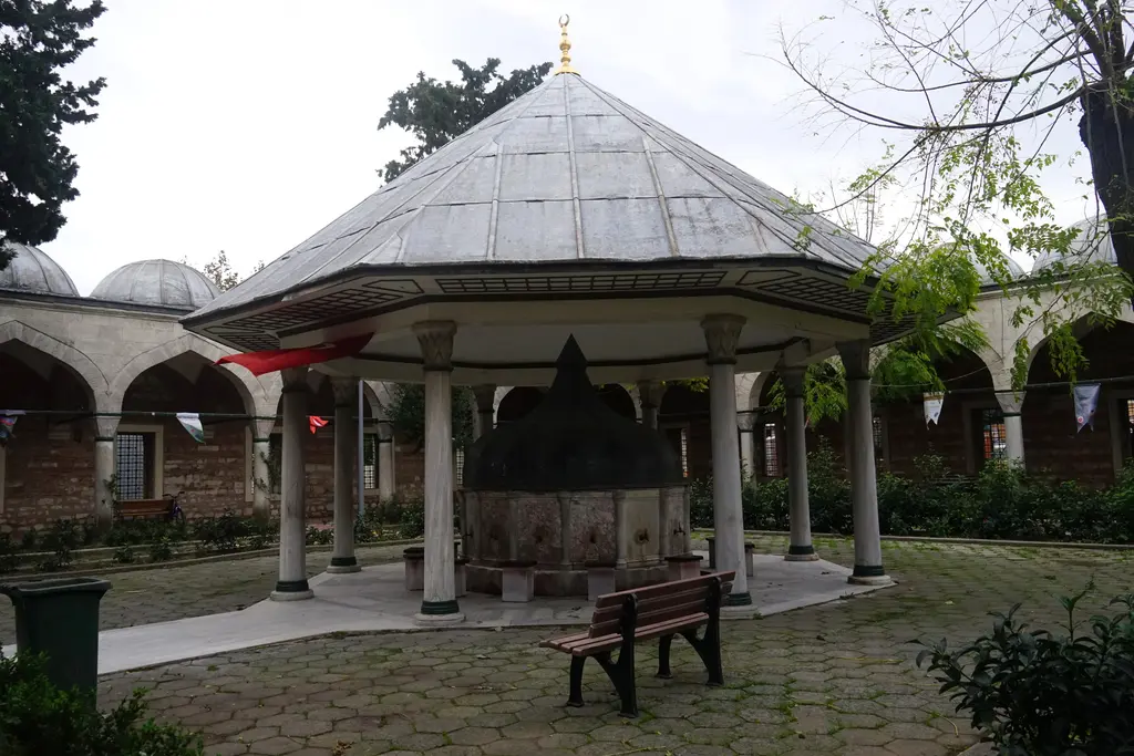 Nişancı Mehmed Paşa Camii'nin avlusunda şadırvan; kurşun kaplı piramidal çatı, ince sütunlar, ortada taş hazne ve yanında bank.