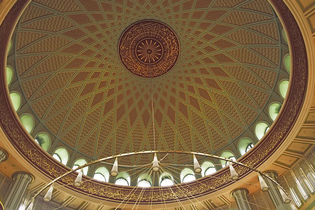 Taksim Camii'nin kubbesi; aşağıdan bakışta altın ve kırmızı tonlu geometrik bezeme, kasnakta pencere dizisi ve göbekte yuvarlak hat yazısı.
