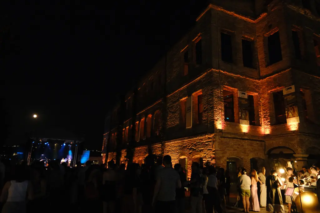 Esma Sultan Yalısı gece; turuncu ve sarı ışıkla yıkanan tuğla cephe, karanlık gökyüzü ve önde kalabalık.