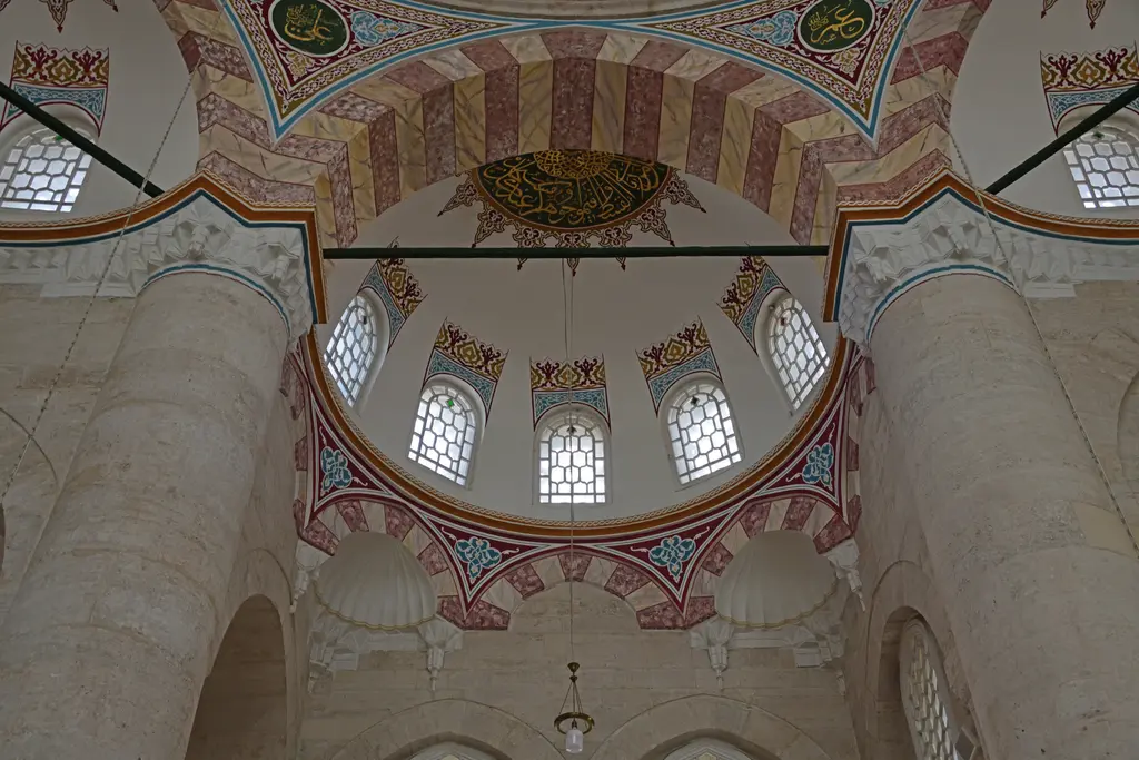 Nişancı Mehmed Paşa Camii'nin içinden kubbeye bakış; iri ayaklar, yarım kubbeler, kırmızı beyaz kemerler ve kasnaktaki pencere dizisi.