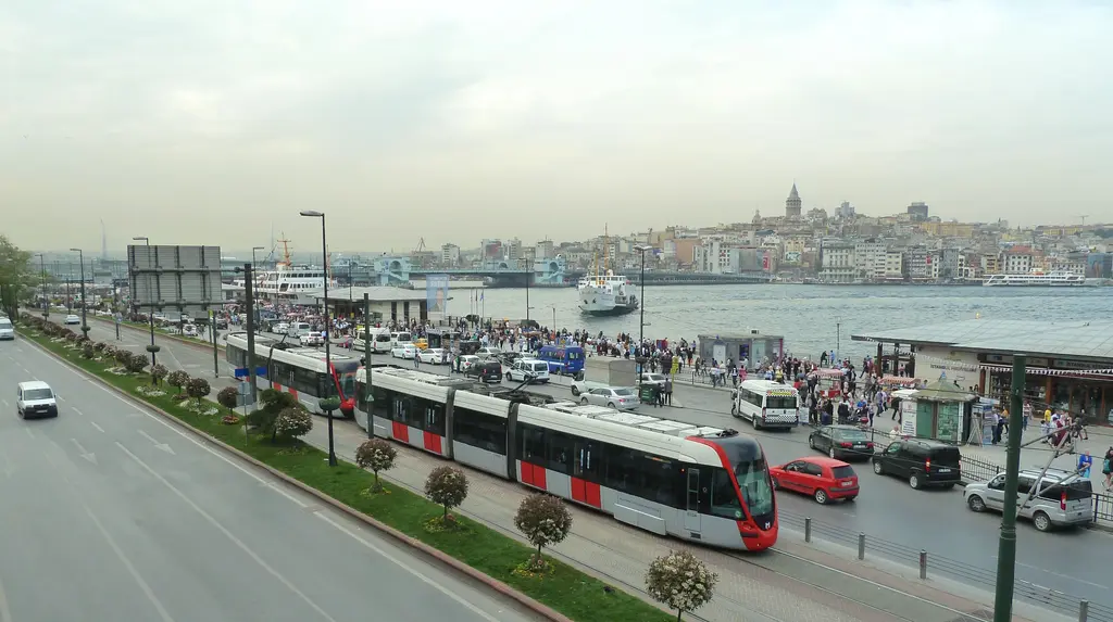 Eminönü kıyısında T1 tramvayı; kırmızı beyaz tramvay, rıhtım boyunca yol, iskeleler ve karşıda Galata.