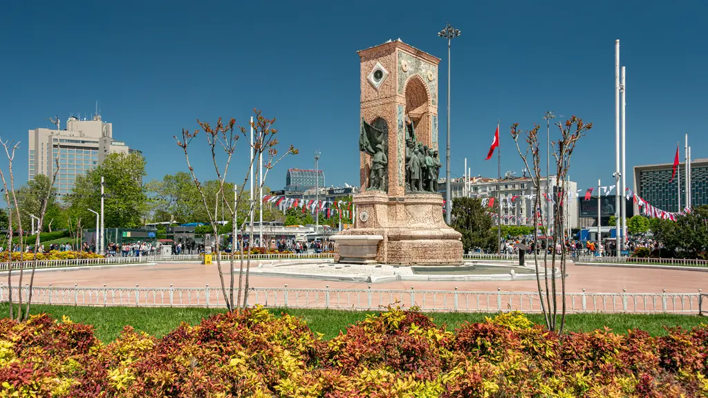 Taksim Meydanı'nda Cumhuriyet Anıtı; önde turuncu ve kırmızı çiçek tarhları, arkada ağaçlar ve açık mavi gökyüzü.