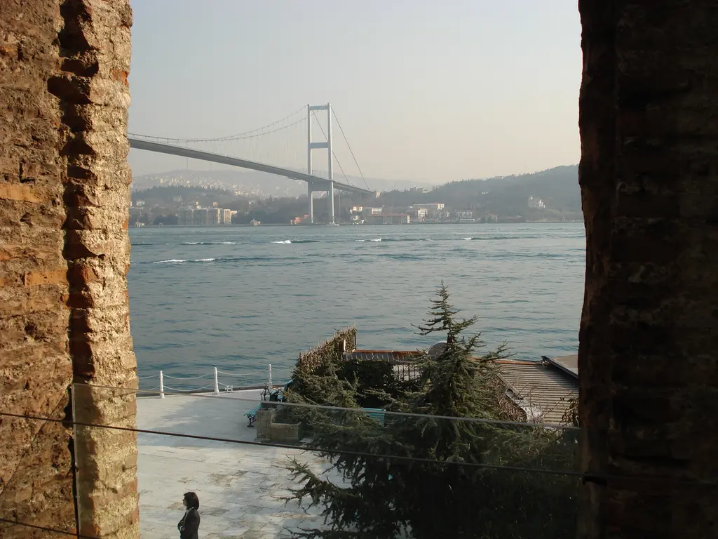 Esma Sultan Yalısı'nın duvar boşluğundan Boğaz; tuğla pervaz, ağaçlar, rıhtım ve uzakta asma köprü.