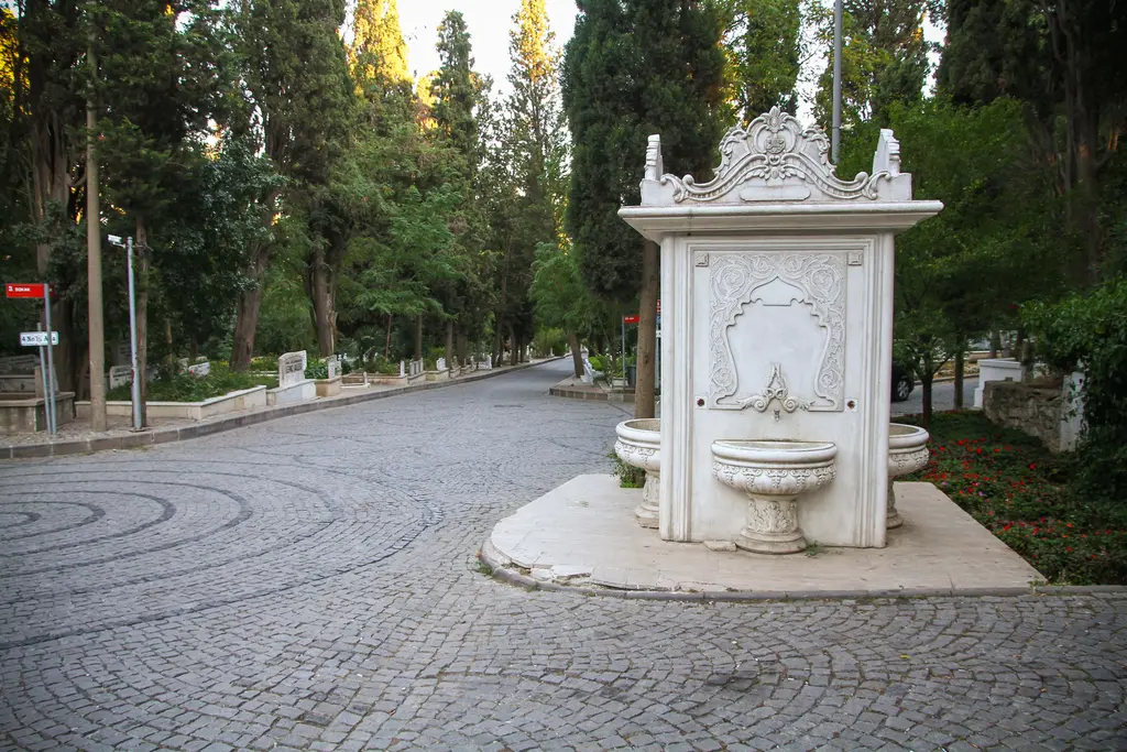 Karacaahmet'te mermer çeşme; kabartmalı beyaz mermer ayna, iki yanında sütunçeler, önünde yalak ve çevresinde selviler.