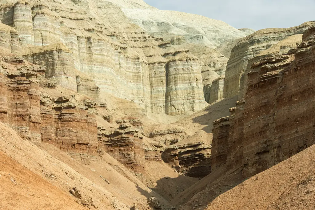 Altyn-Emel'de Aktau Dağları; yatay şeritler hâlinde beyaz, krem ve pembe katmanlar taşıyan aşınmış yamaçlar ve önlerindeki kuru vadi tabanı.