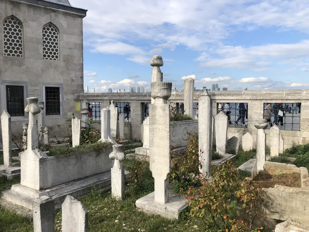 Şemsi Paşa Camii'nin haziresi; sarıklı ve düz mezar taşları, mermer sandukalar, arkada cami duvarı.