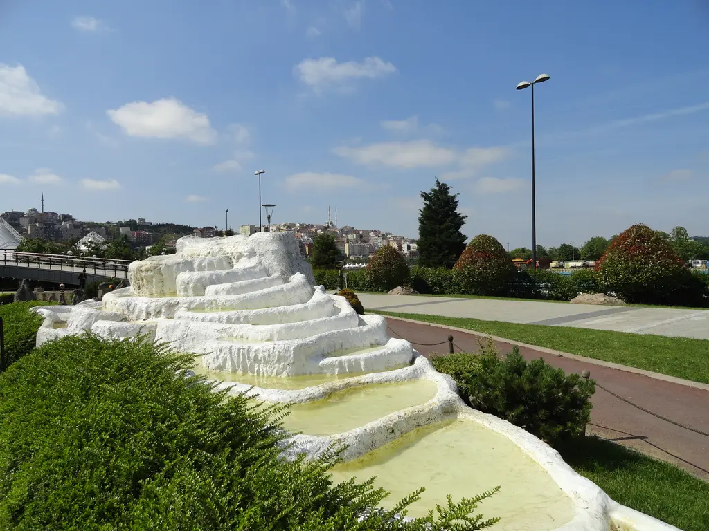 Miniatürk'te Pamukkale maketi; beyaz basamaklı travertenler, havuzlarda açık sarı yeşil su, önde çit, sağda kırmızı tuğla yol.
