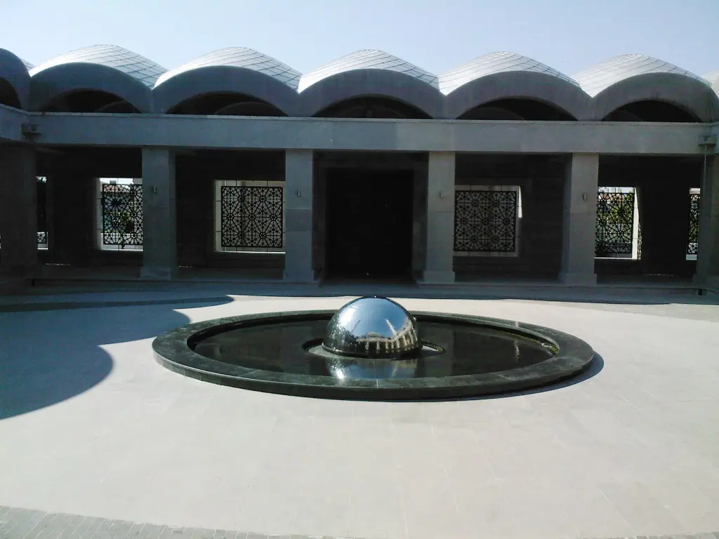 Şakirin Camii'nin avlusu; ortada siyah havuz içinde parlak çelik küreli şadırvan, arkada kemer dizili revaklar.