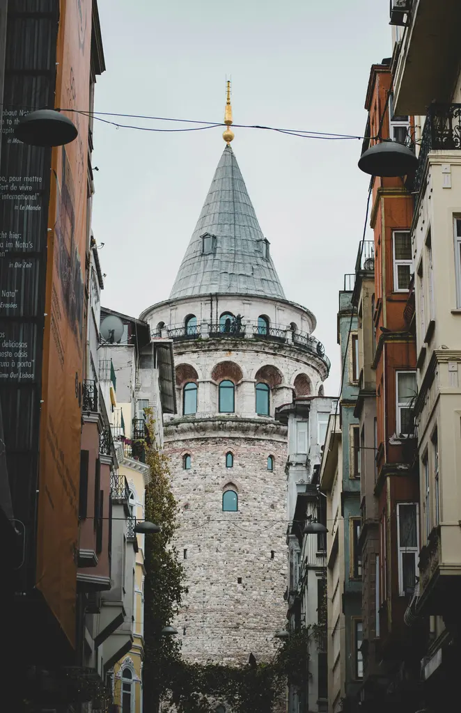 Beyoğlu'nda dar bir sokağın ucunda Galata Kulesi; iki yandaki yüksek cepheler, sarkan fenerler ve kulenin gri külahı.