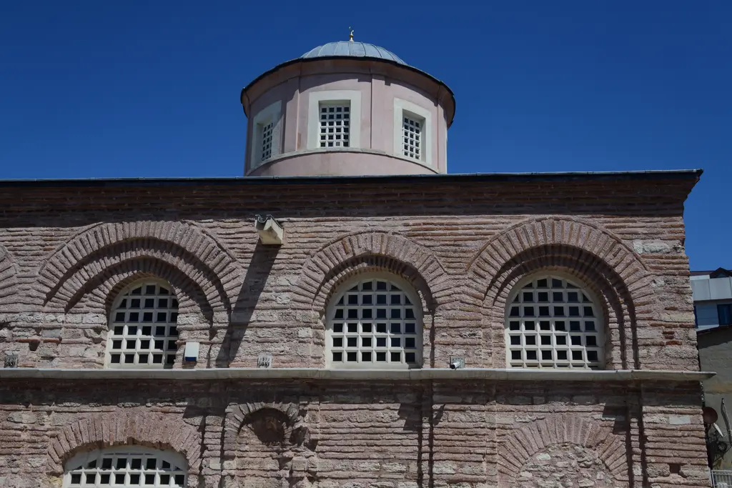 Fenari İsa Camii'nin kubbe kasnağı mavi gök altında; pembe sıvalı silindirik kasnak, kurşun külah ile alem, altta beyaz mermer şebekeli üç kemerli pencere.