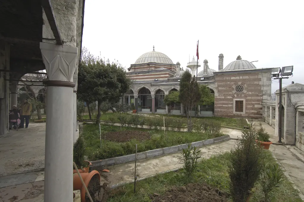 Şemsi Paşa Külliyesi'nin avlusu; revak sütunu, bahçedeki ağaçlar, patika ve arkada caminin kubbesi.