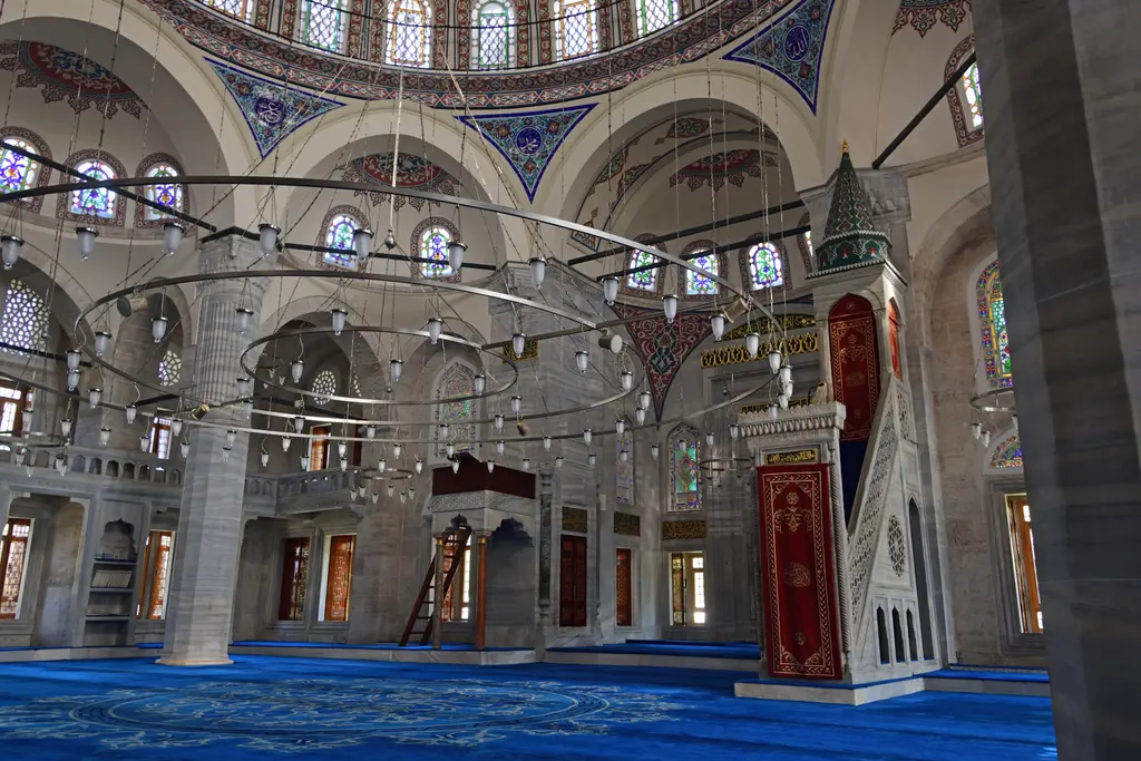 Azapkapı Sokullu Mehmed Paşa Camii'nin içi; taş kemerler ve payeler, alçakta asılı avize çemberleri, mavi halı ve renkli camlı pencereler.