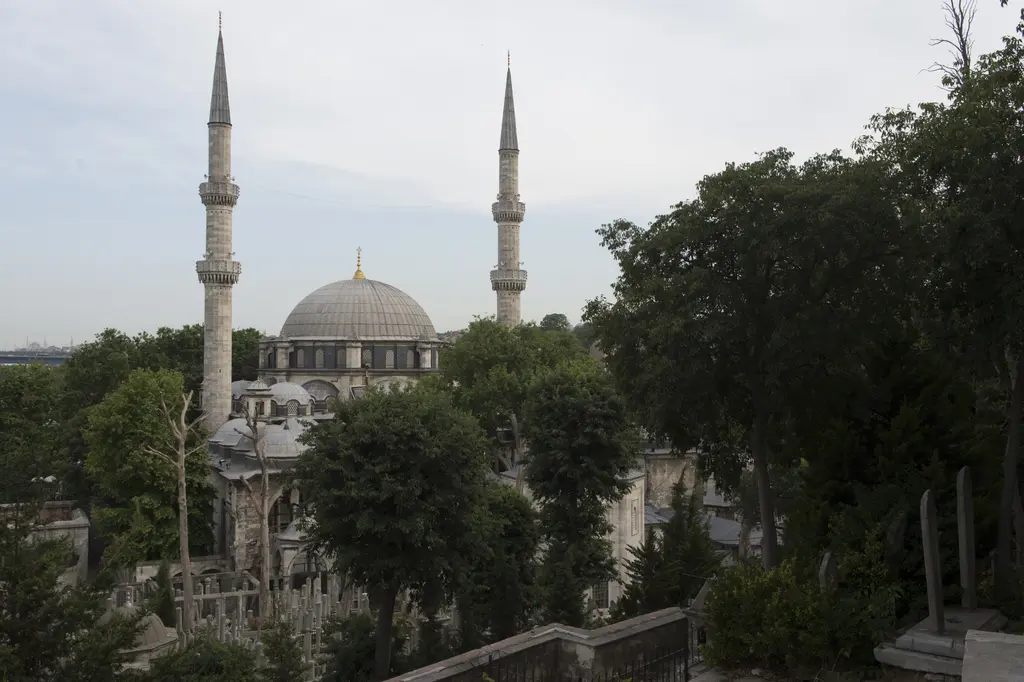 Eyüp Sultan Camii; yamaçtan bakışla kubbe, iki minare, avlu revakları ve önündeki yeşil ağaçlar.