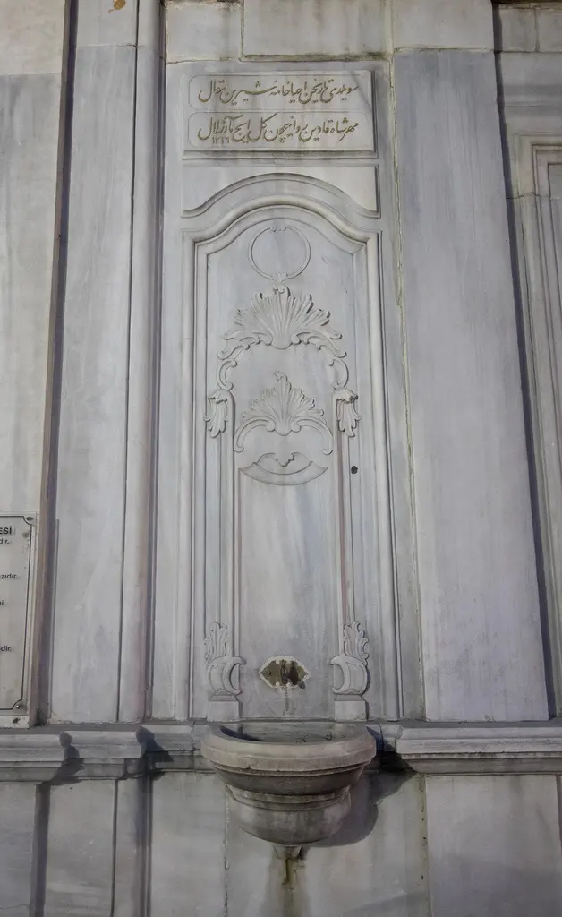 Şah Sultan Türbesi'nin çeşmesi; mermer duvarda kabartmalı ayna taşı, üstte iki satırlık kitabe ve oval yalak.