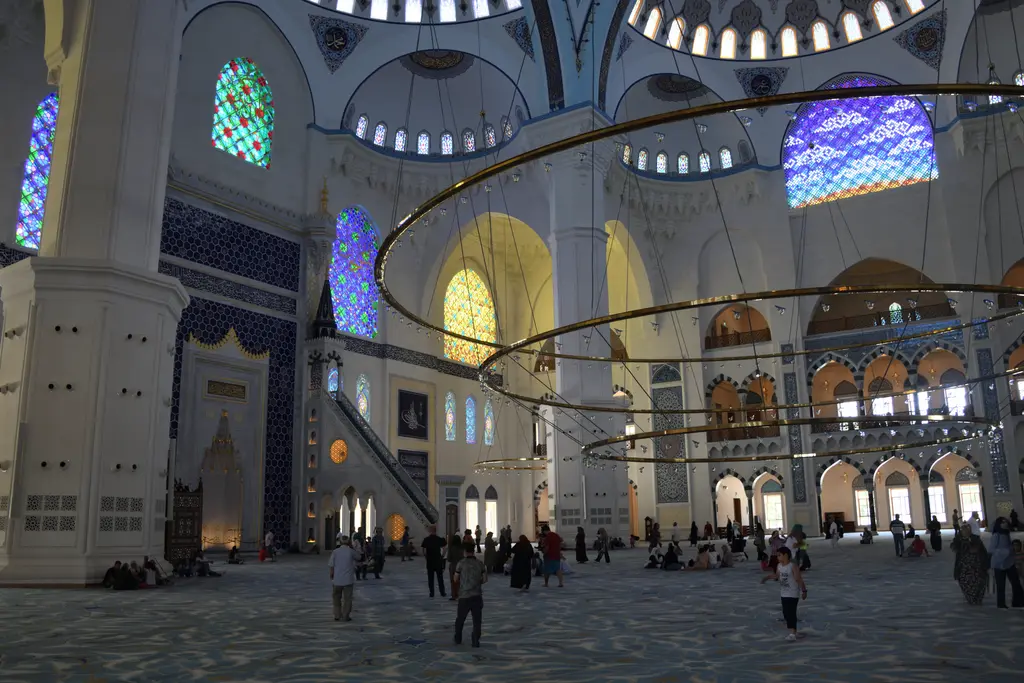 Büyük Çamlıca Camii'nin harimi; halka avizeler, renkli camlı pencereler ve uzakta lacivert çinili mihrap duvarı.