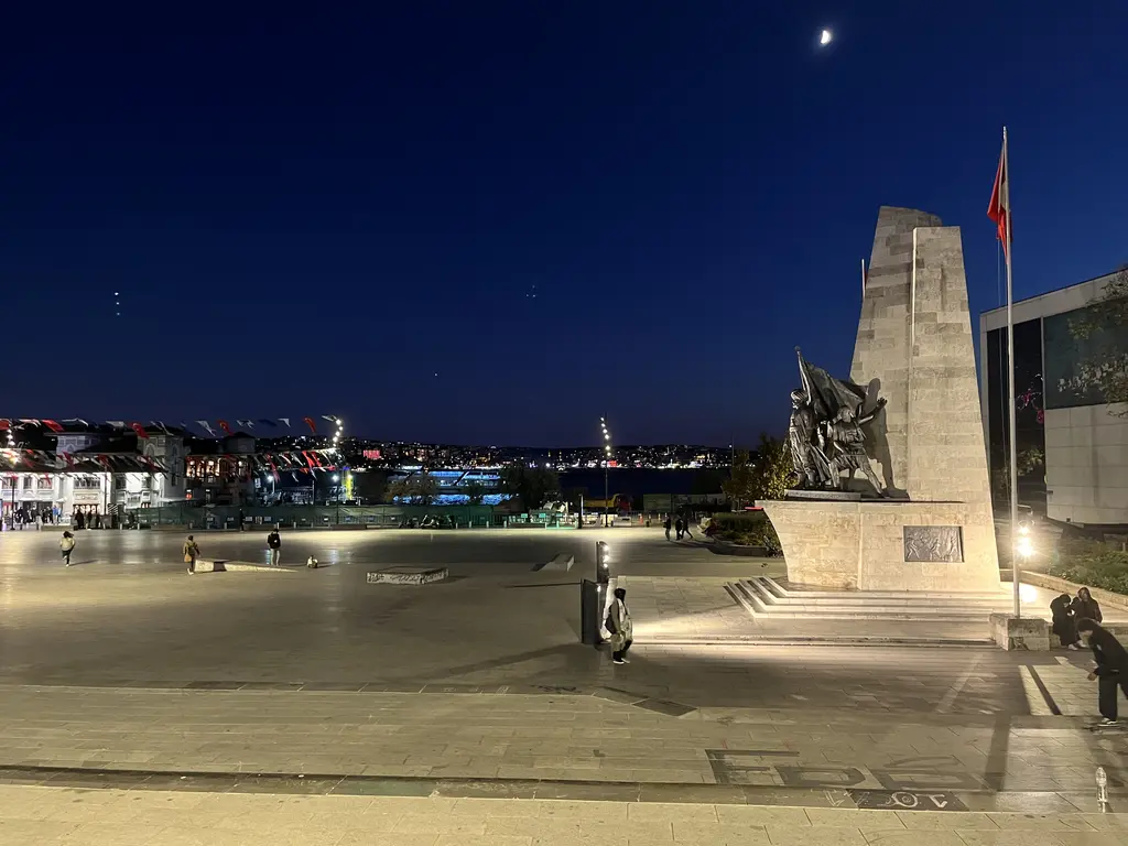 Beşiktaş'ta gece Barbaros Anıtı; aydınlatılmış taş kaide, bayrak, geniş meydan ve arkada Boğaz'ın ışıkları.