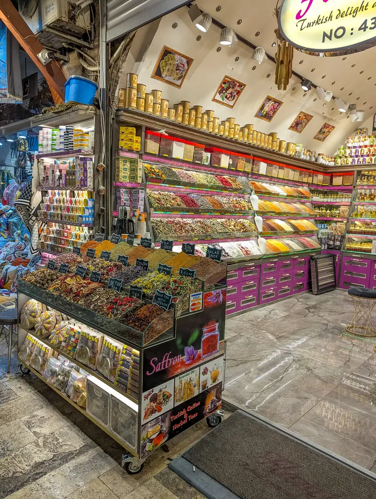 Arasta Çarşısı'nda baharat dükkânı; tezgâhta yığın yığın lokum ve baharat, raflarda renkli paketler, ışıklı tabela ve mermer zemin.