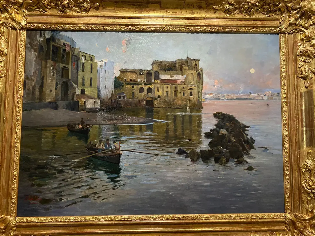 Gaetano Esposito'nun Napoli Körfezi tablosu; kıyıdaki eski taş yapılar, sakin su, kayıklar ve uzakta sisli ufuk.