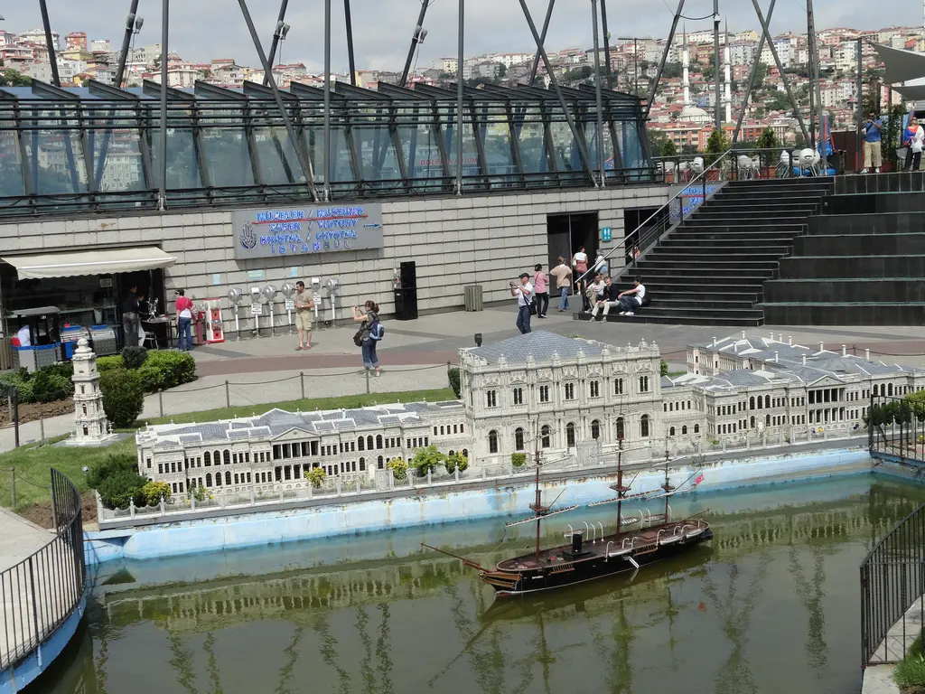 Miniatürk'te Dolmabahçe Sarayı maketi; havuz kenarında uzun beyaz cephe, suda üç direkli bir gemi maketi, arkada camlı giriş binası.