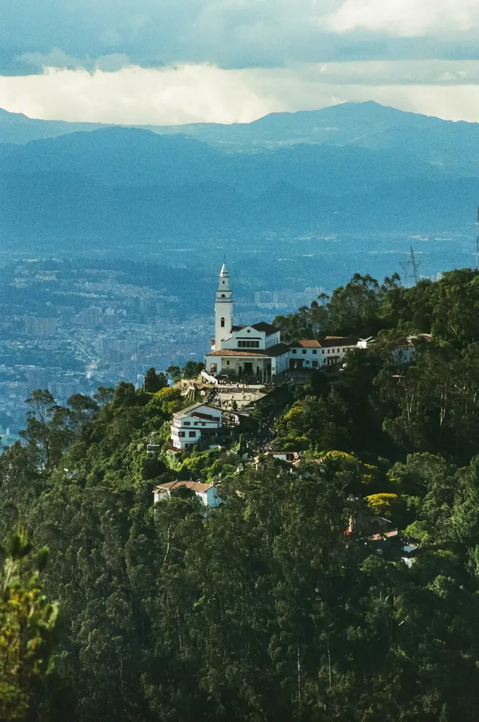 Kolombiya'nın başkenti Bogotá'ya tepeden bakan Monserrate; ormanlık yamacın üstündeki beyaz kilise ve manastır, arkada uzanan geniş kent ile dağlar.