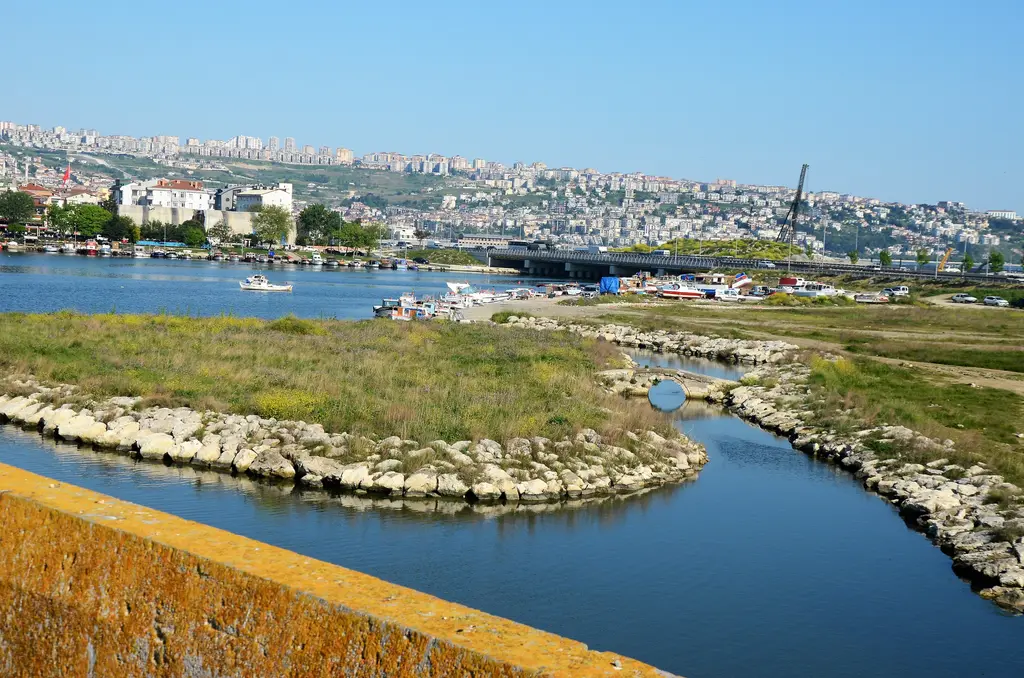 Kanuni Sultan Süleyman Köprüsü'nden gölün ağzı; kıvrılan kanal, yeşil adacıklar, taş kıyılar ve uzakta yerleşim.