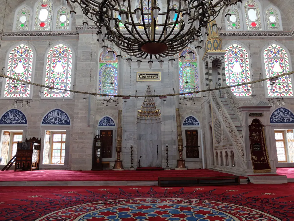 Mihrimah Sultan Camii'nin harimi mihraba doğru; kırmızı halı, alçak asılan avize halkası, iki yanda pencere sıraları, mihrap ve mermer minber.