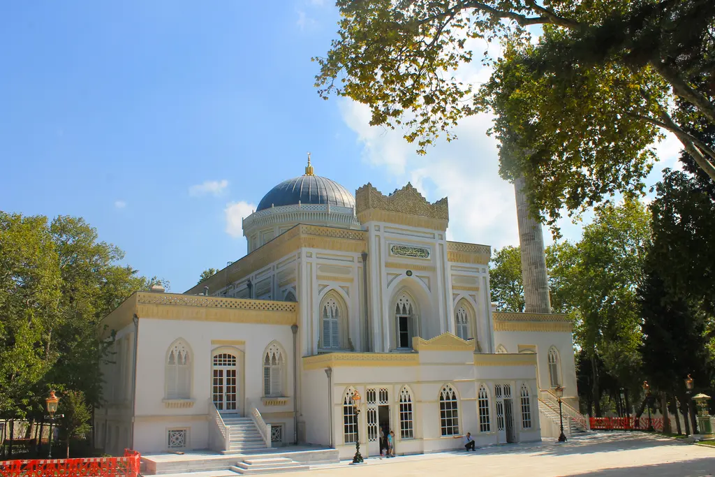 Beşiktaş'ta Yıldız Hamidiye Camii; beyaz ve sarı cephe, mavi kurşun kubbe, sivri kemerli pencereler, ince minare ve çevresinde ağaçlar.