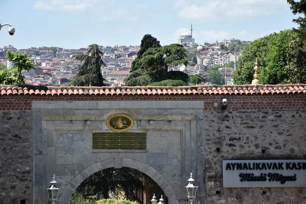 Aynalıkavak Kasrı'nın bahçe kapısı; taş duvar üzerinde mermer kemerli kapı, üstünde tuğra ve kitabe, sağda müze tabelası.