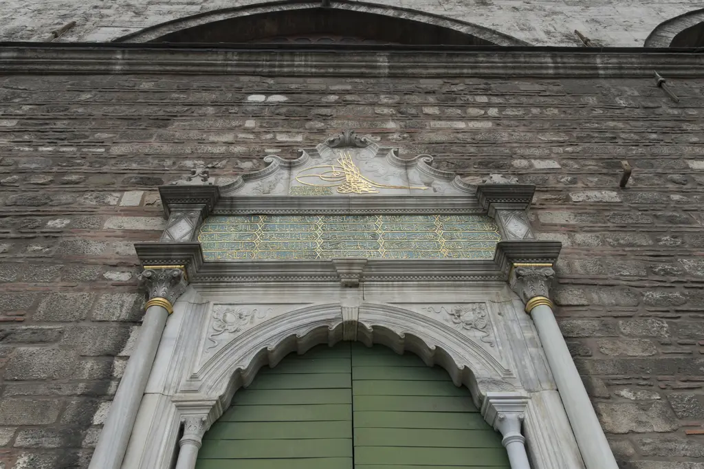 Tophane-i Âmire'de mermer çerçeveli kapı; yeşil boyalı ahşap kanatlar, üstünde kitabe panosu ve iki yanında taş duvar.